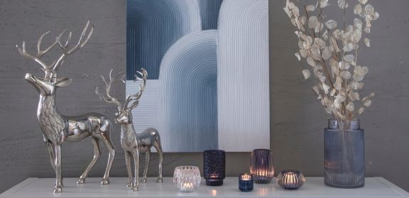 Sideboard dekoriert mir silbernen Hirschen, verschiedenen Teelichthaltern und einer Vase mit Dekogesteck. Alles ist in silber und blau gehalten.