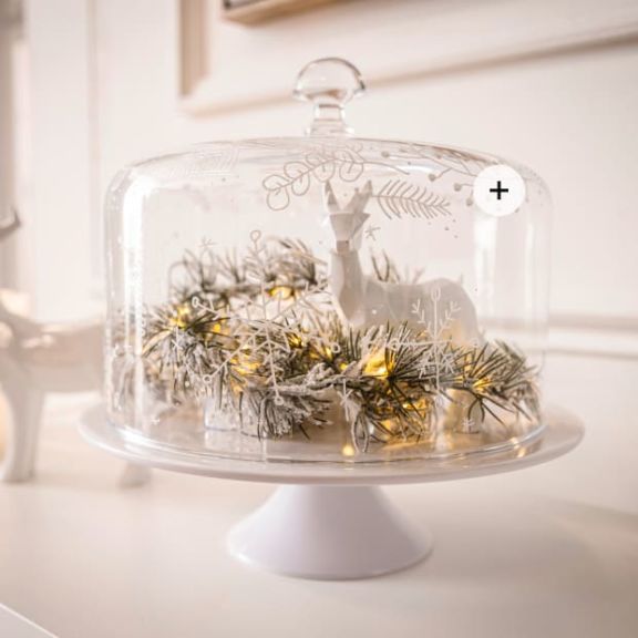Cloche auf Tortenplatte, innen dekoriert mit einer weißen Rehfigur und einer leuchtenden Zweiggirlande.