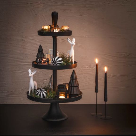 Schwarze Etagere dekoriert mit schwarz weißen Weihnachtskugeln, weißen Hirschen, Kerzen und Tannenzweigen.