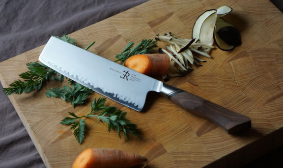 Nakiri-Messer A30 von Ryda Knives mit braunem Holzgriff auf einem Schneidebrett mit Gemüse als Dekoration präsentiert
