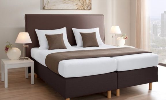 großzügiges Boxspringbett mit weißer Bettwäsche und braunen Kissen
