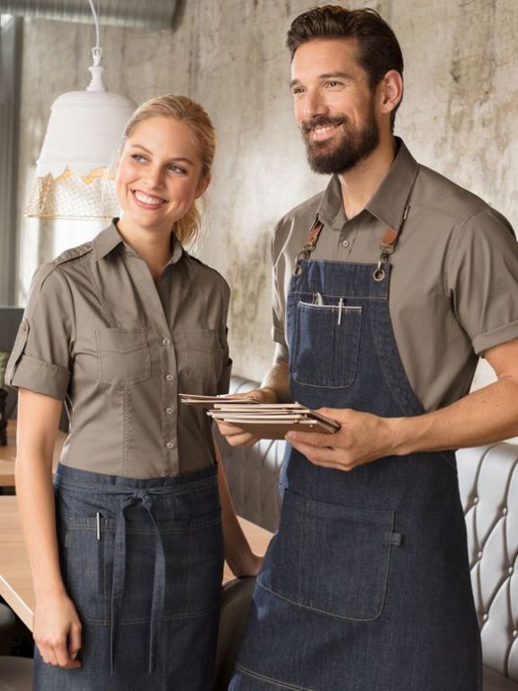 zwei Kellner mit sandfarbenen Hemden und Denimschürzen begrüßen neue Gäste