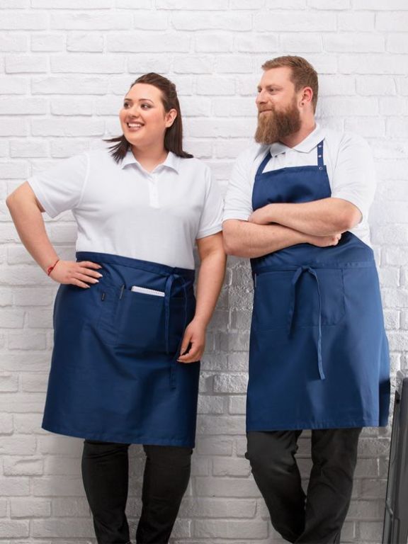 zwie Kellner präsentieren die Servicebekleidung bestehend aus einem weißen Poloshirt, blauer Schürze und schwarzer Stoffhose