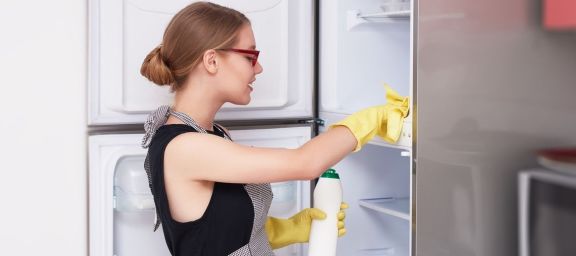 Eine Dame reinigt einen Kühlschrank mit Lappen und Putzmittel