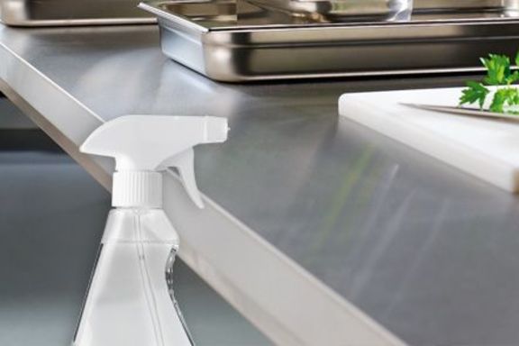 Reinigungsmittel mit Sprühkopf vor Edelstahlküchenzeile