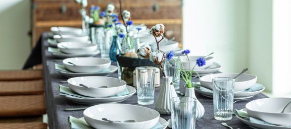 gedeckter Tisch: weisse Teller, Vasen mit blauen Blumen und Baumwollzweigen