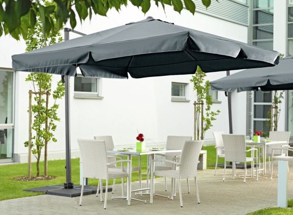 Breva hengeparasoll fra VEGA på en grå terrasse med hvite stoler