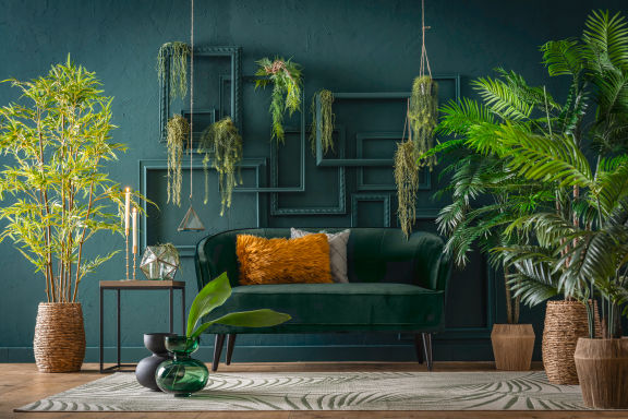 Schönes grünes Sofa mit Dekokissen, Dekopflanzen, Vasen, grüne Wand mit grünen Bilderrahmen