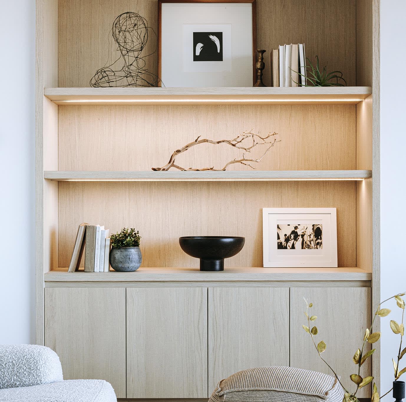  A light wood built-in shelving unit with three open shelves and two lower cabinets. 
