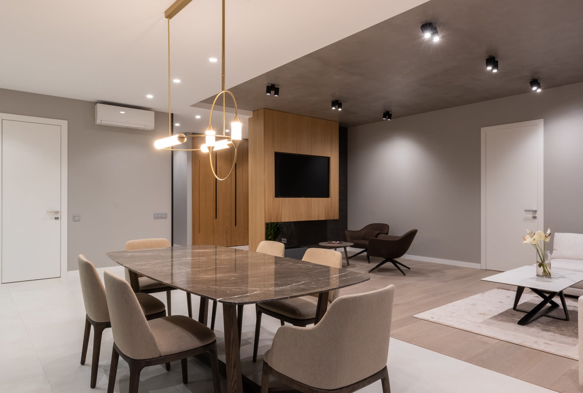 A living room with an airy space, modern pieces of furniture, a chandelier, and a doorway leading to another room.