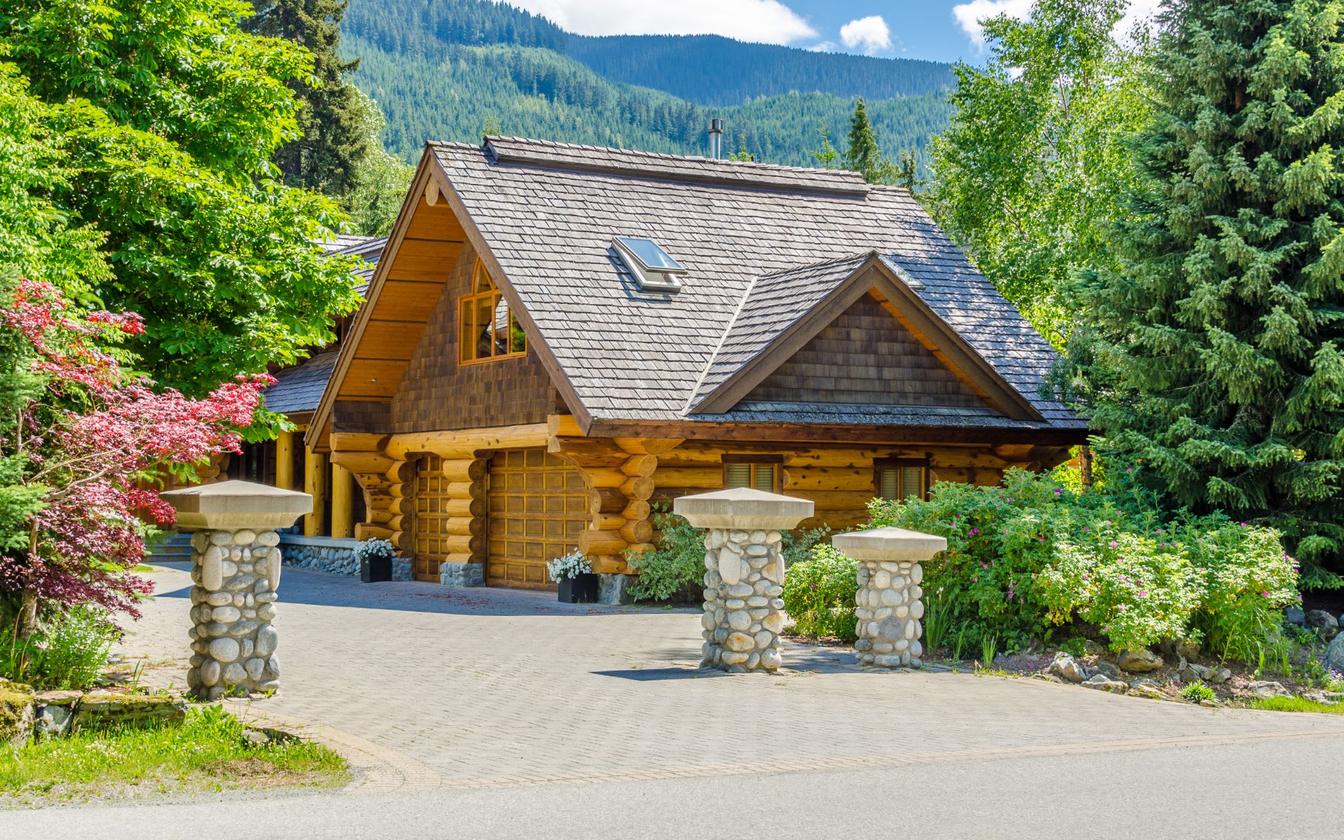 A large log cabin in the woods, with a porch, a balcony, and a chimney