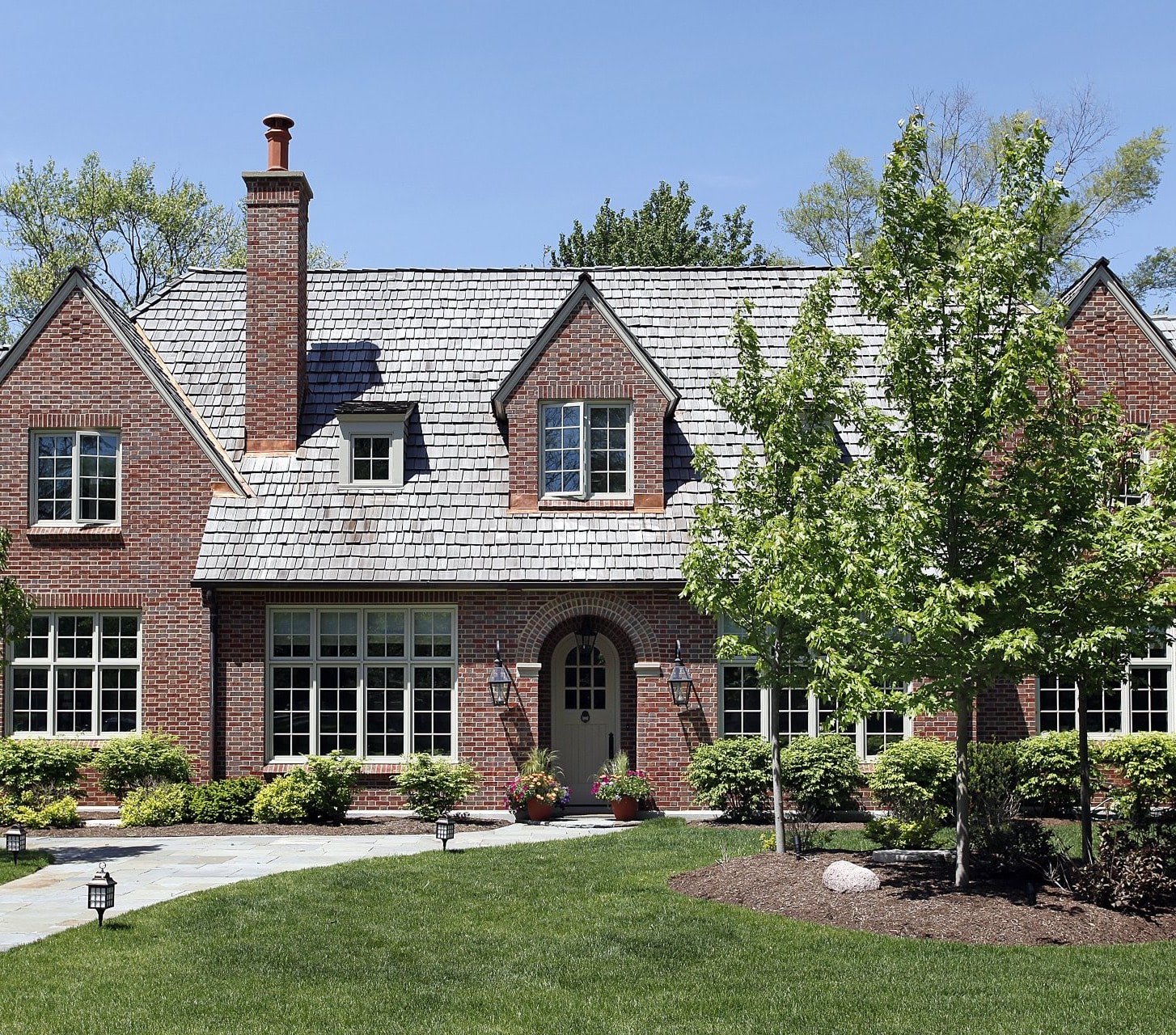 A large, two-story brick house with a cedar shake roof and a central chimney