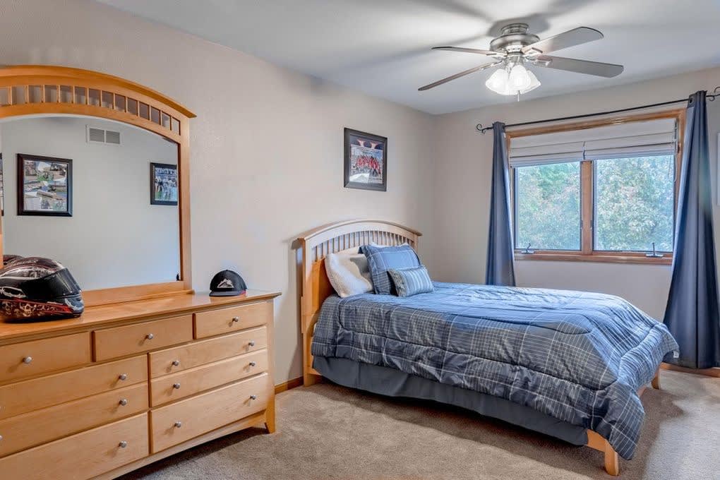 Bedroom with a full-size bed, patterned comforter, wooden dresser, ceiling fan, and windows showing the outside view.