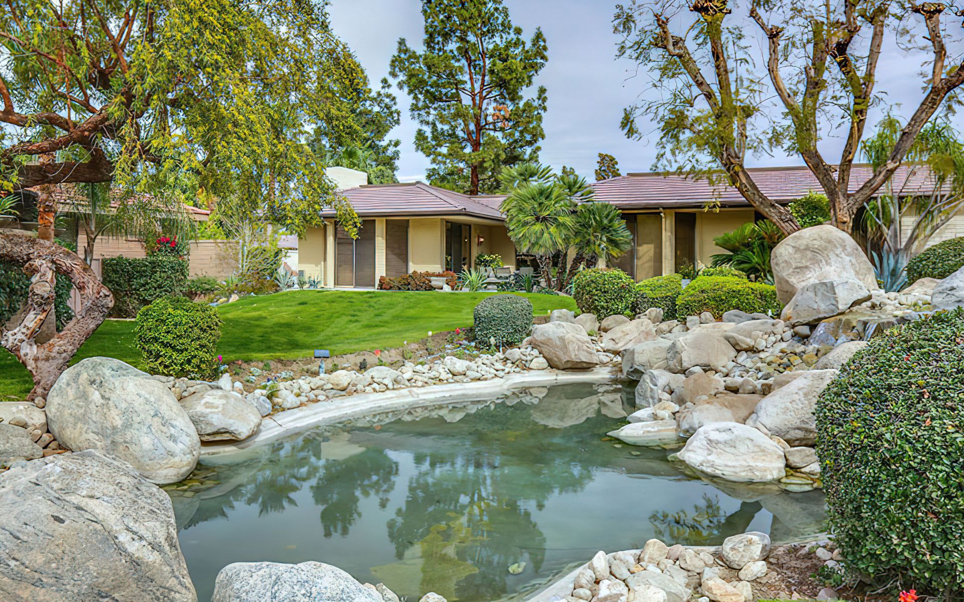 A backyard oasis with a pond, rocks, and lush greenery surrounding a quaint house