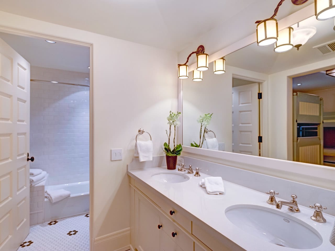 A bathroom with two sinks, a large mirror, and a bathtub in the background