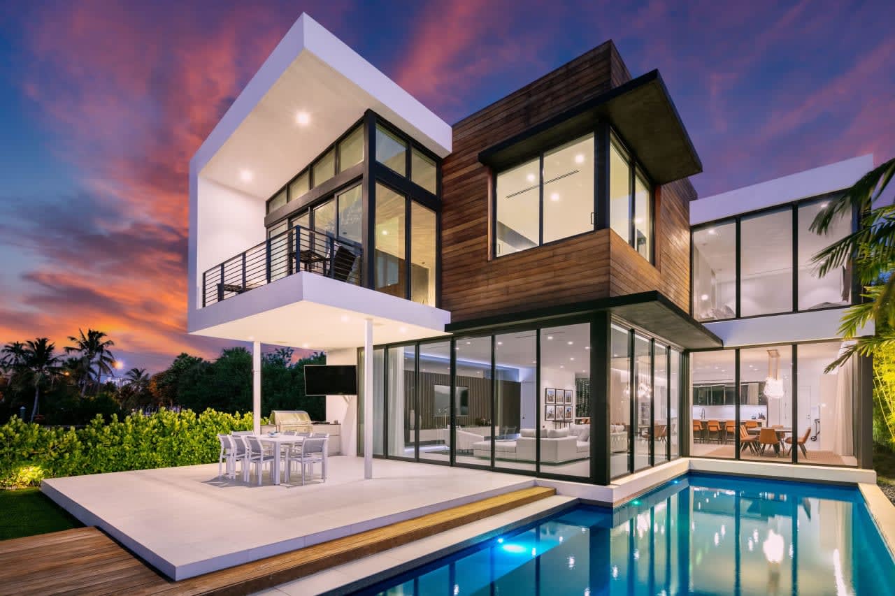 A modern house with a swimming pool and a deck at sunset. The house is made of wood and has a glass facade