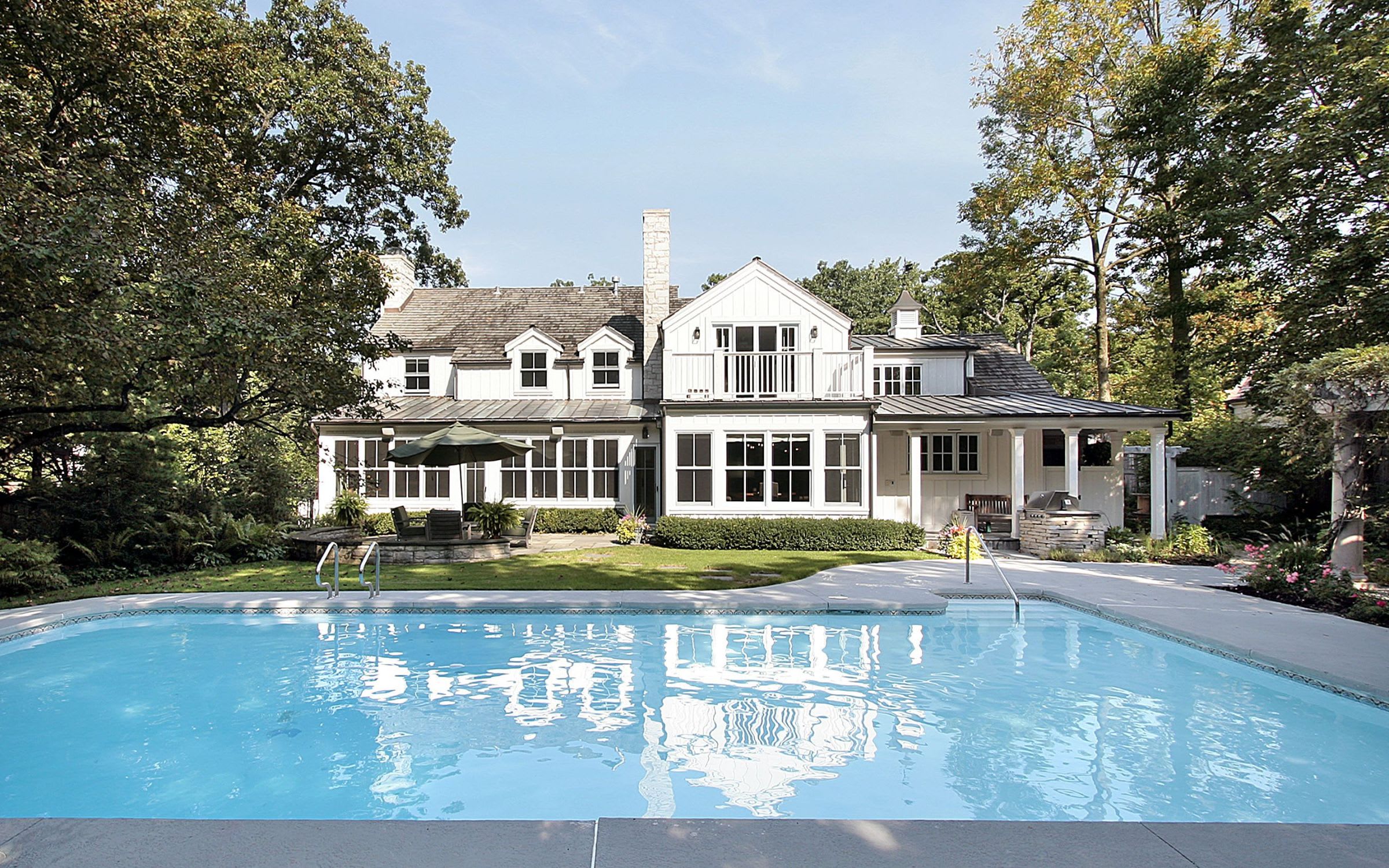 A large white house with a gray roof and black shutters sits on a spacious lawn