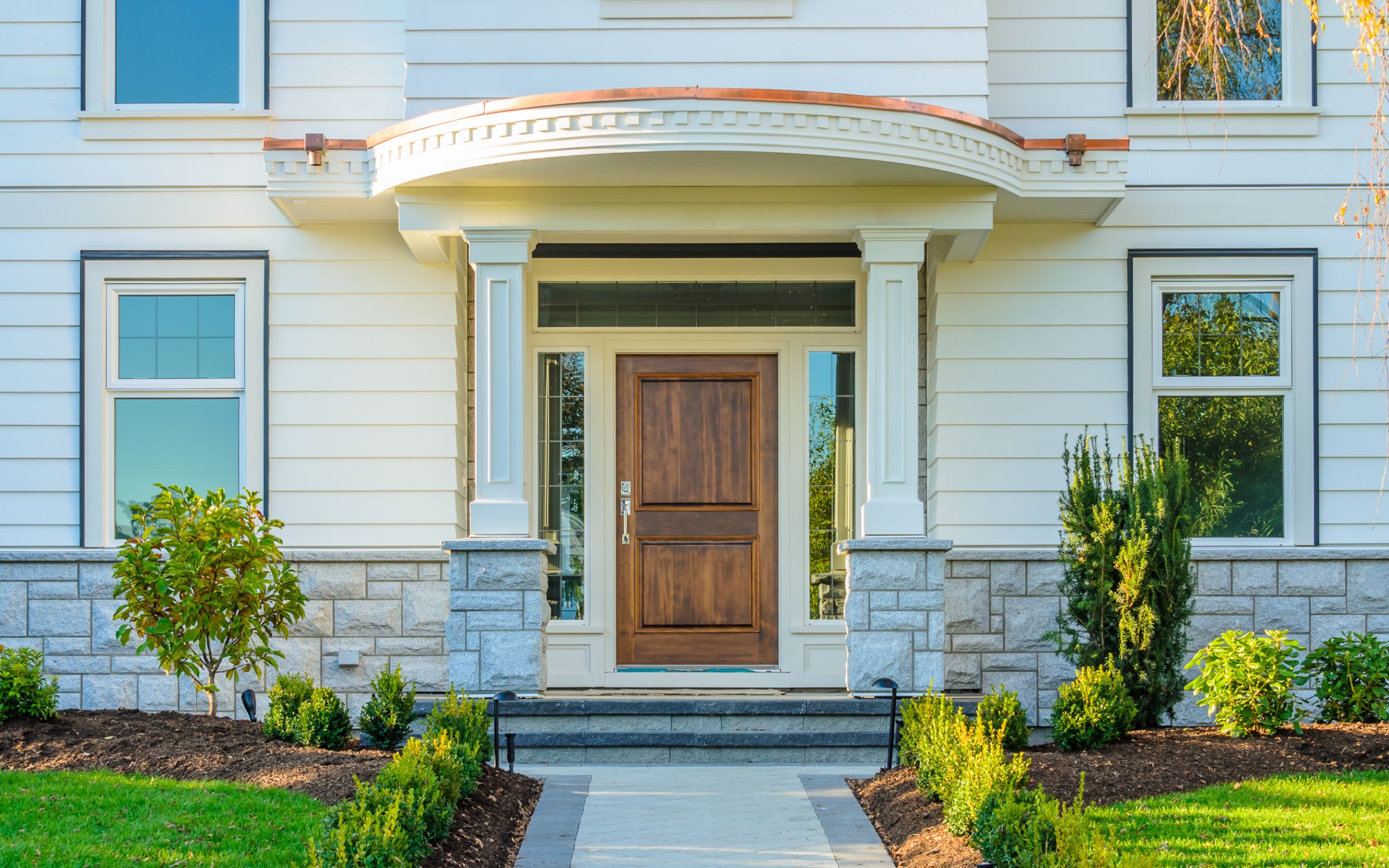 The front door of a white house with a wooden door and two windows flanking it.