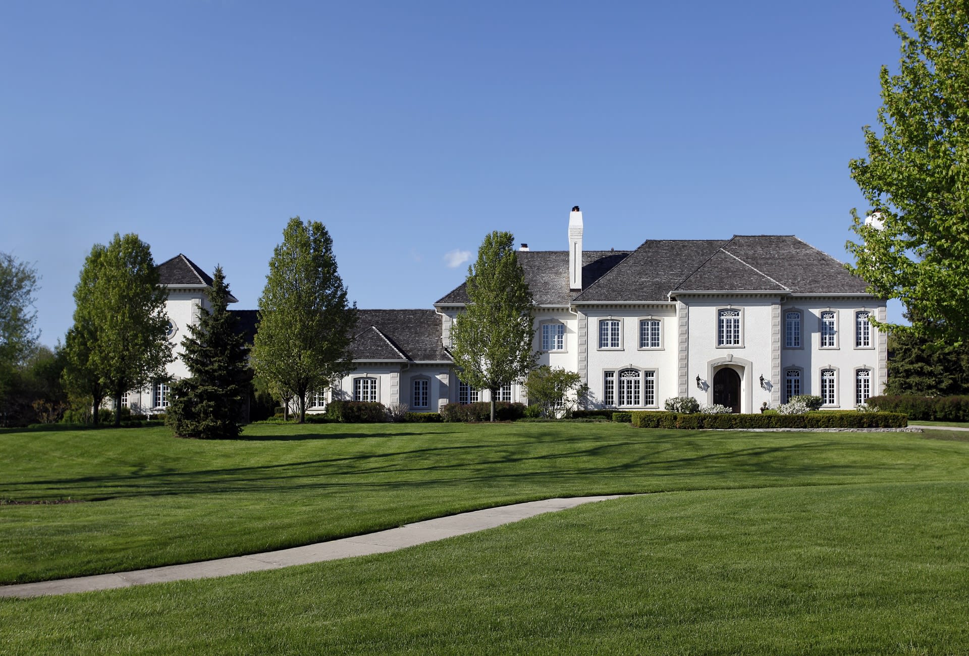 A grand Georgian-style mansion with a covered porch, white gazebo, curved driveway, trees, hedges, and well-maintained lawn.