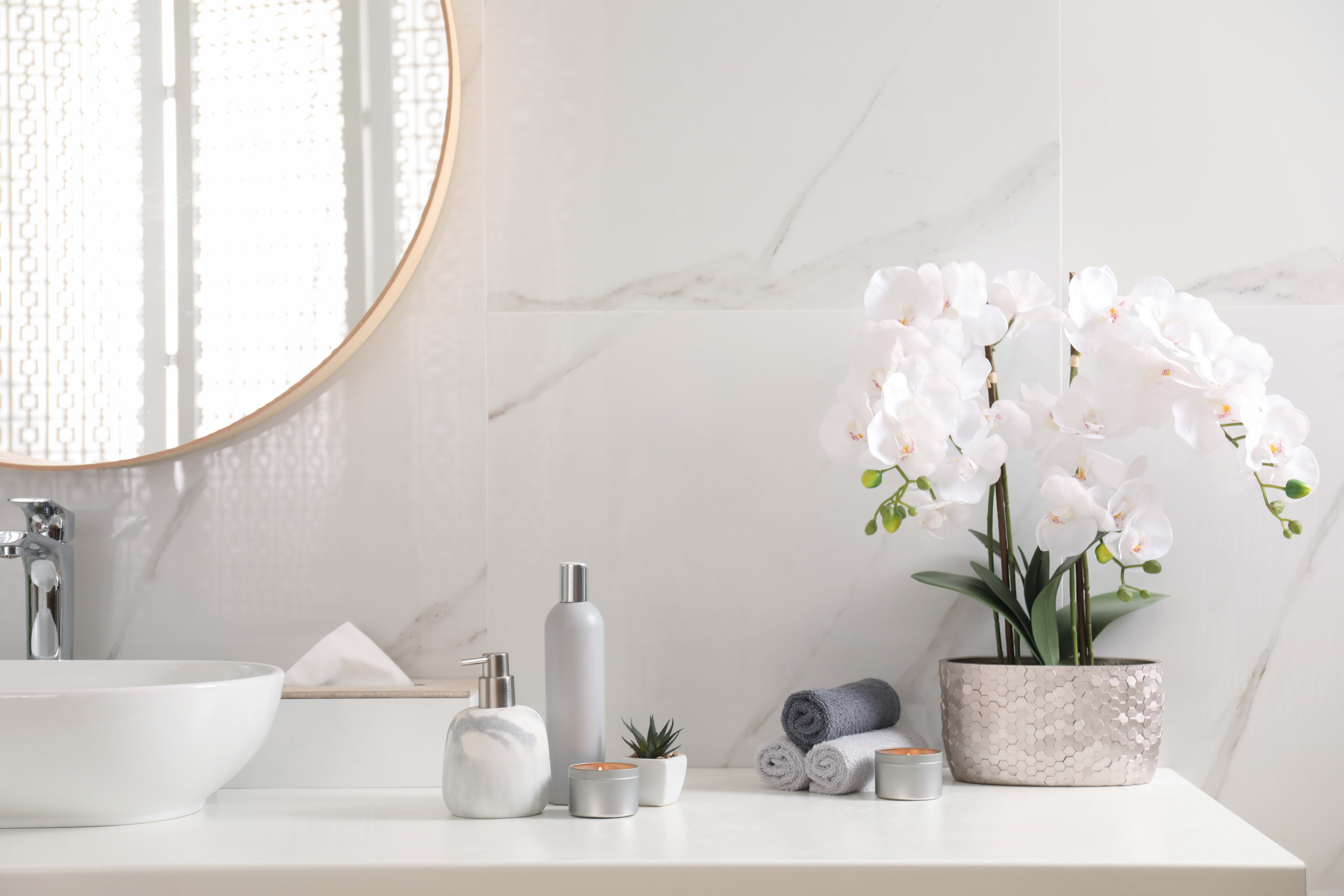 A bathroom vanity with a white countertop, a sink, a rectangular mirror, a vase with white flowers, and folded towels.