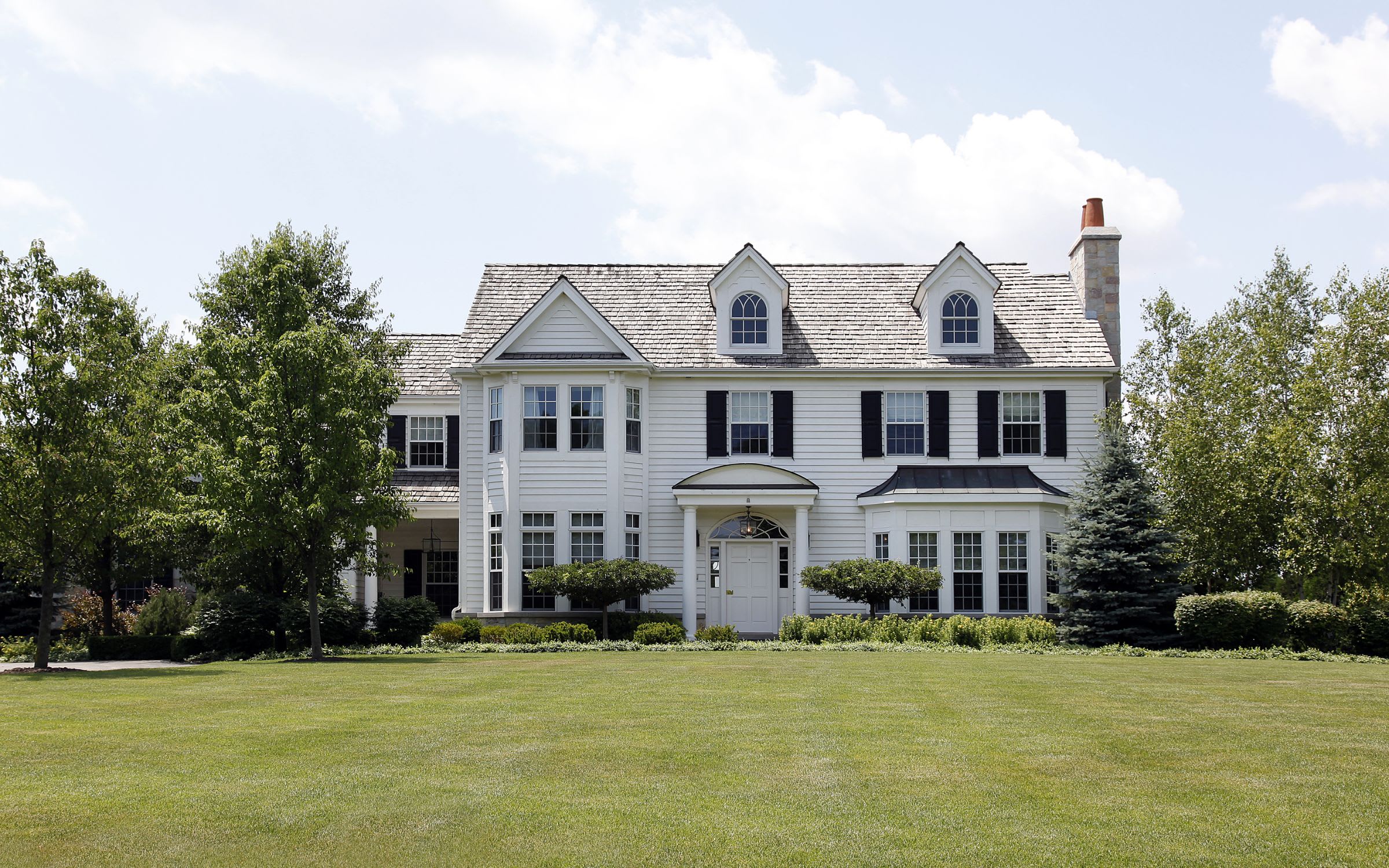 A large white house with black shutters sitting on a lush green lawn.