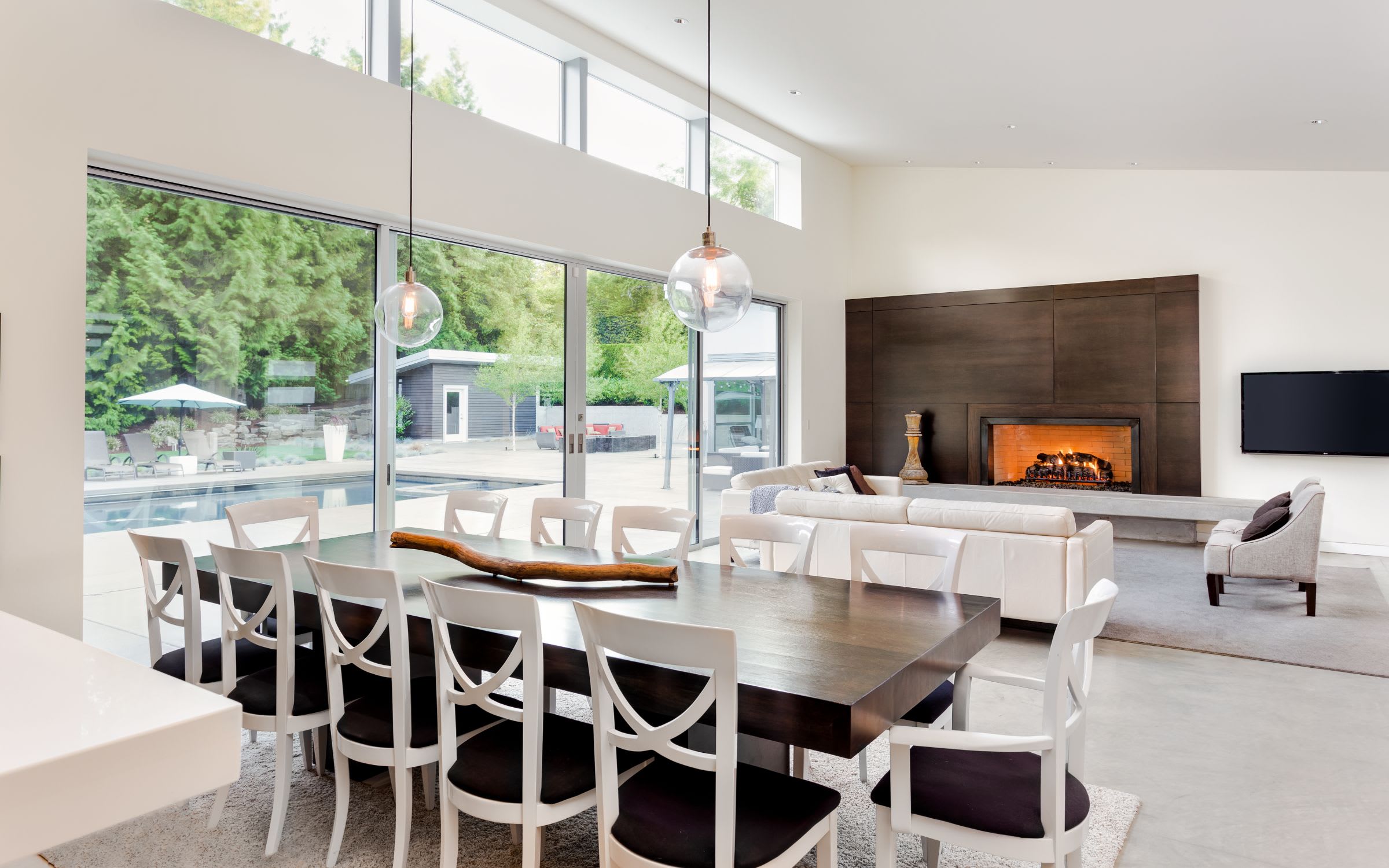 A modern, open-concept living room and dining room with white walls and large windows