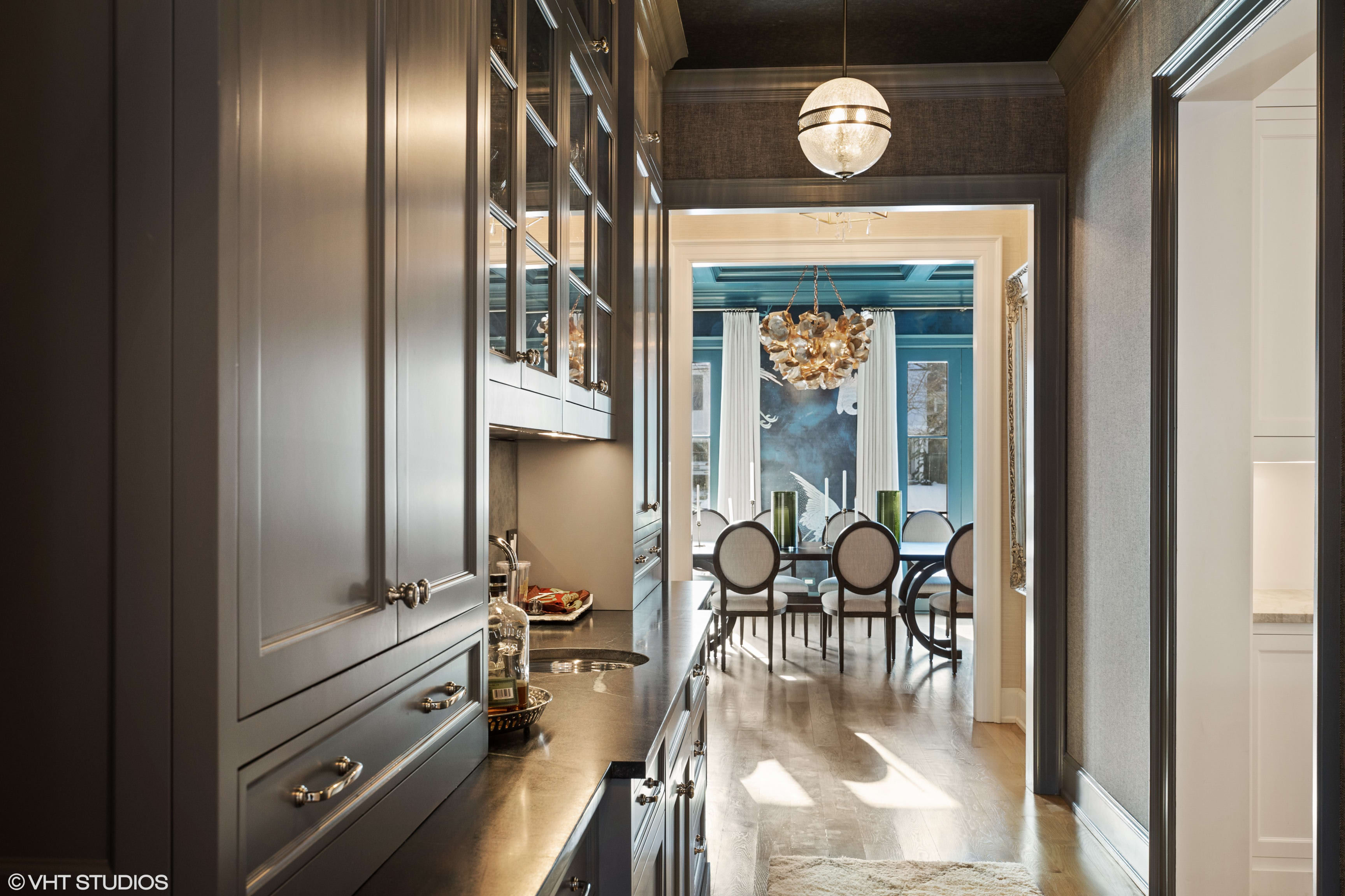 A pantry with a sink, cabinets, and countertops, leading to a dining room