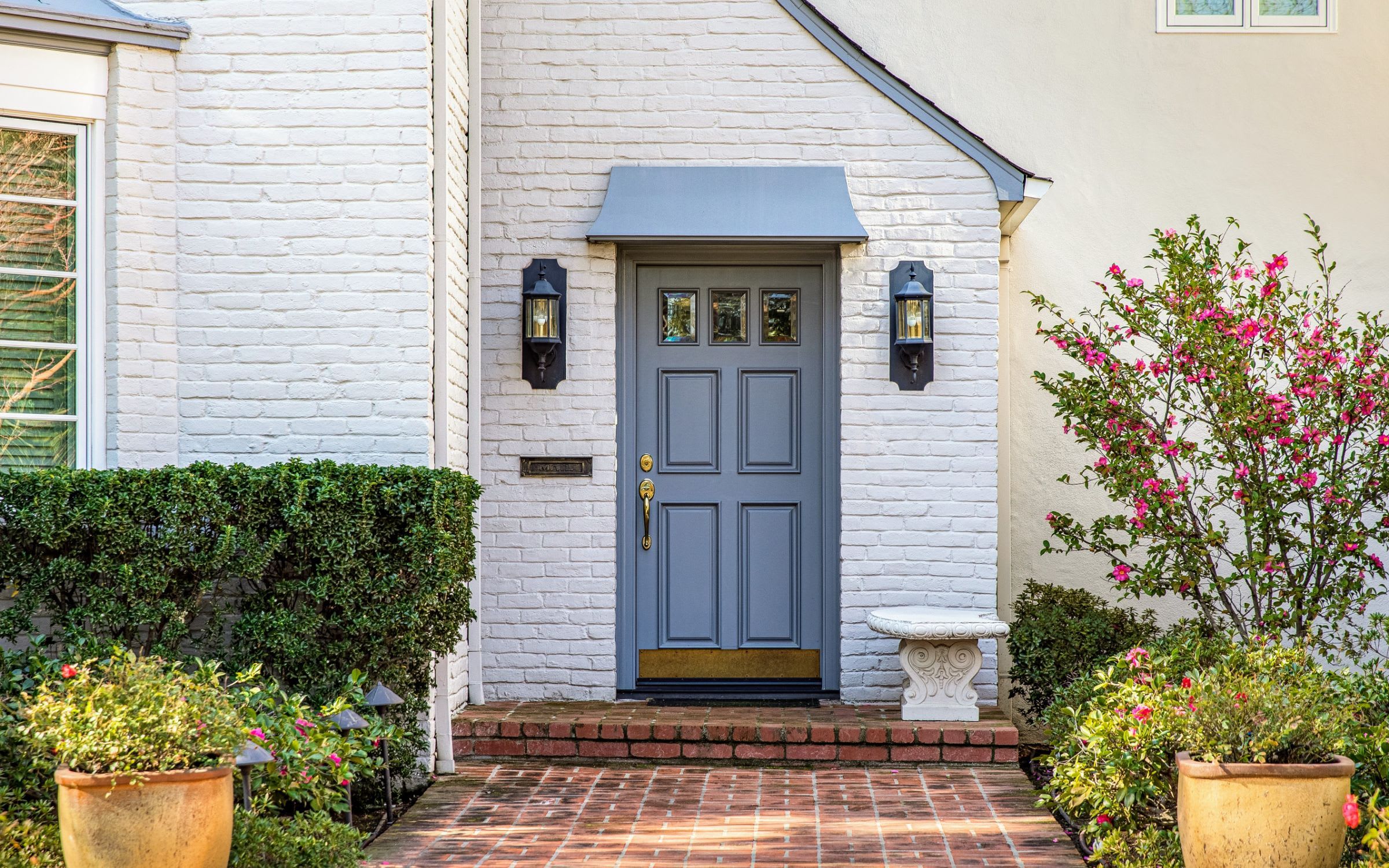 A white brick house with a blue door and a brick walkway.