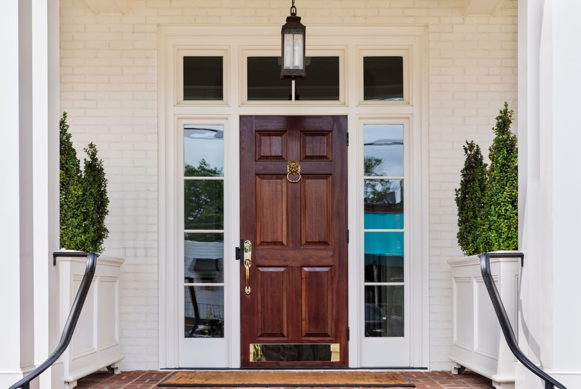 A close-up of a wooden front door with a brass door knocker, two vertical panels, and white plant boxes on both sides.