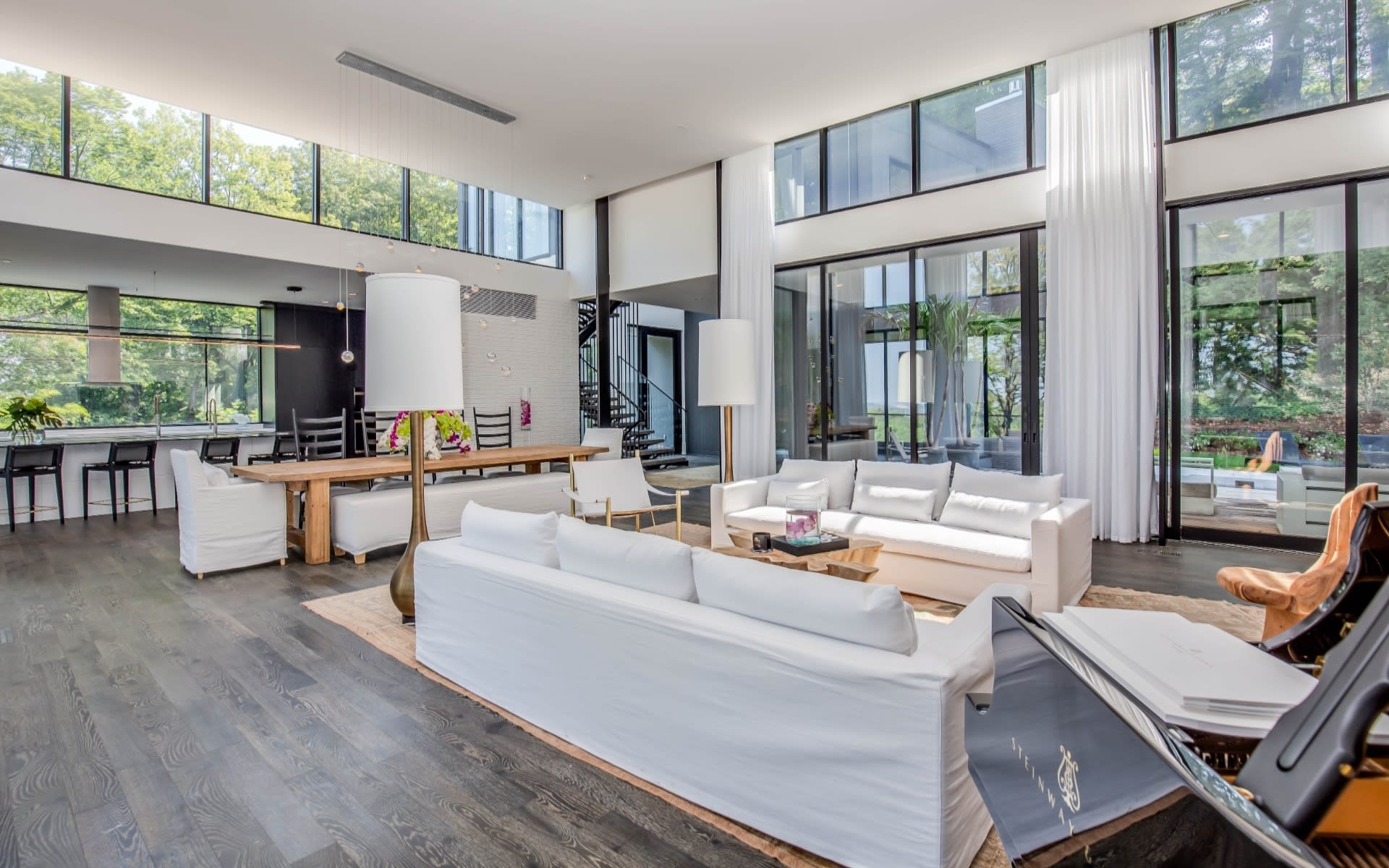 A comfortably furnished living room with a white couch, two white chairs, a white piano, and a coffee table