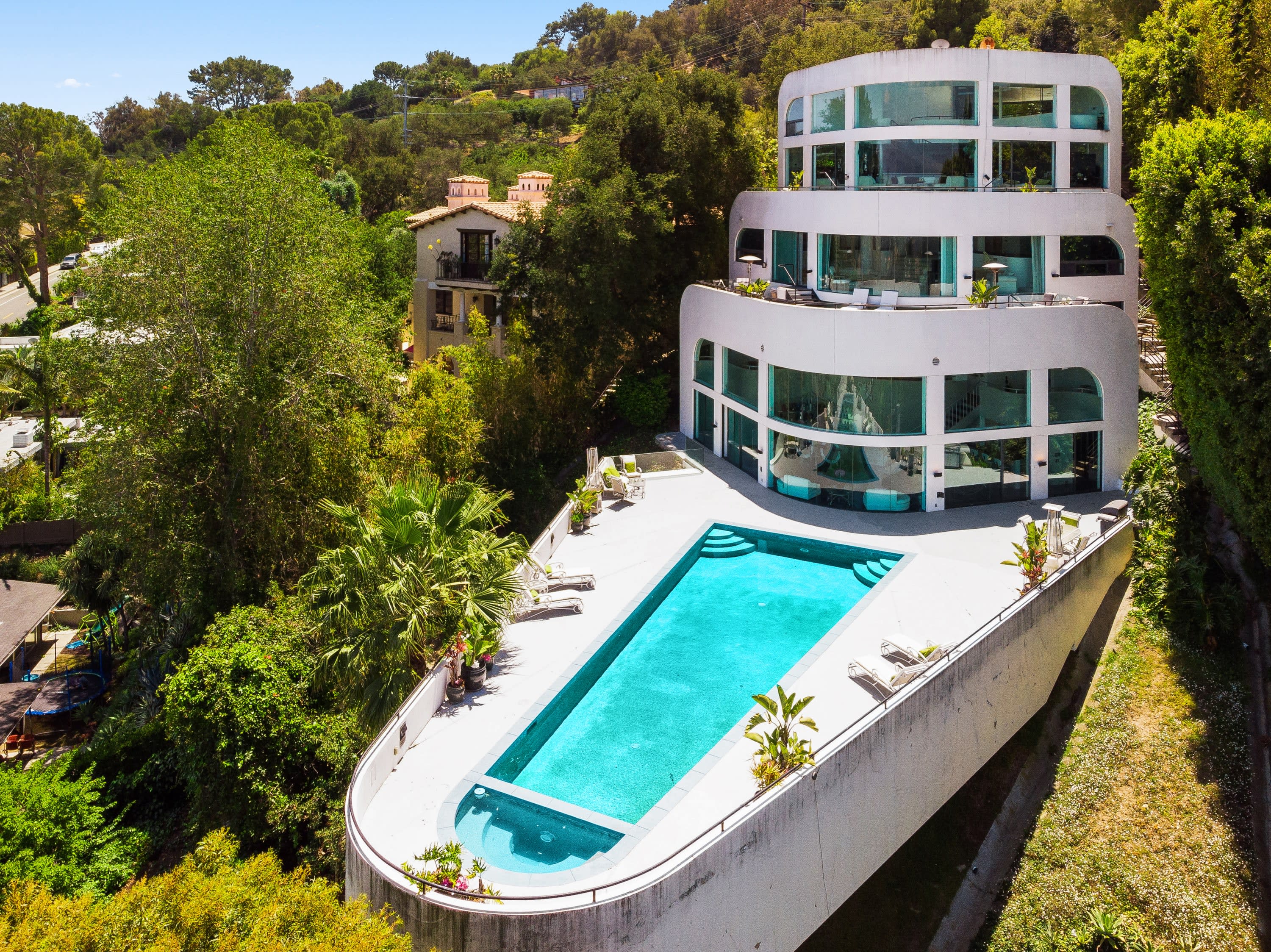 A large modern house with a white exterior and a swimming pool surrounded by trees