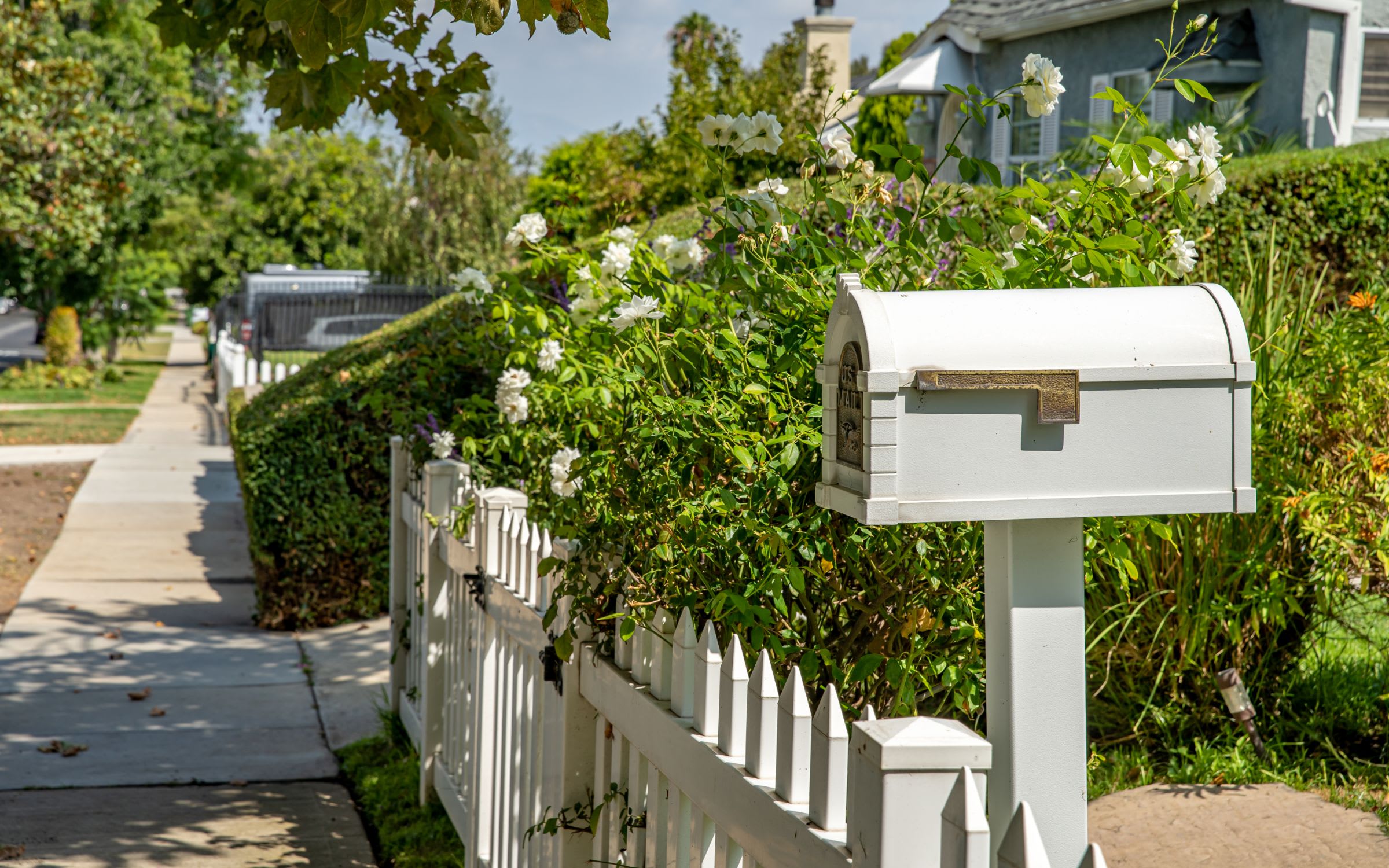 A white mailbox standing next to a white picket fence in a suburban neighborhood