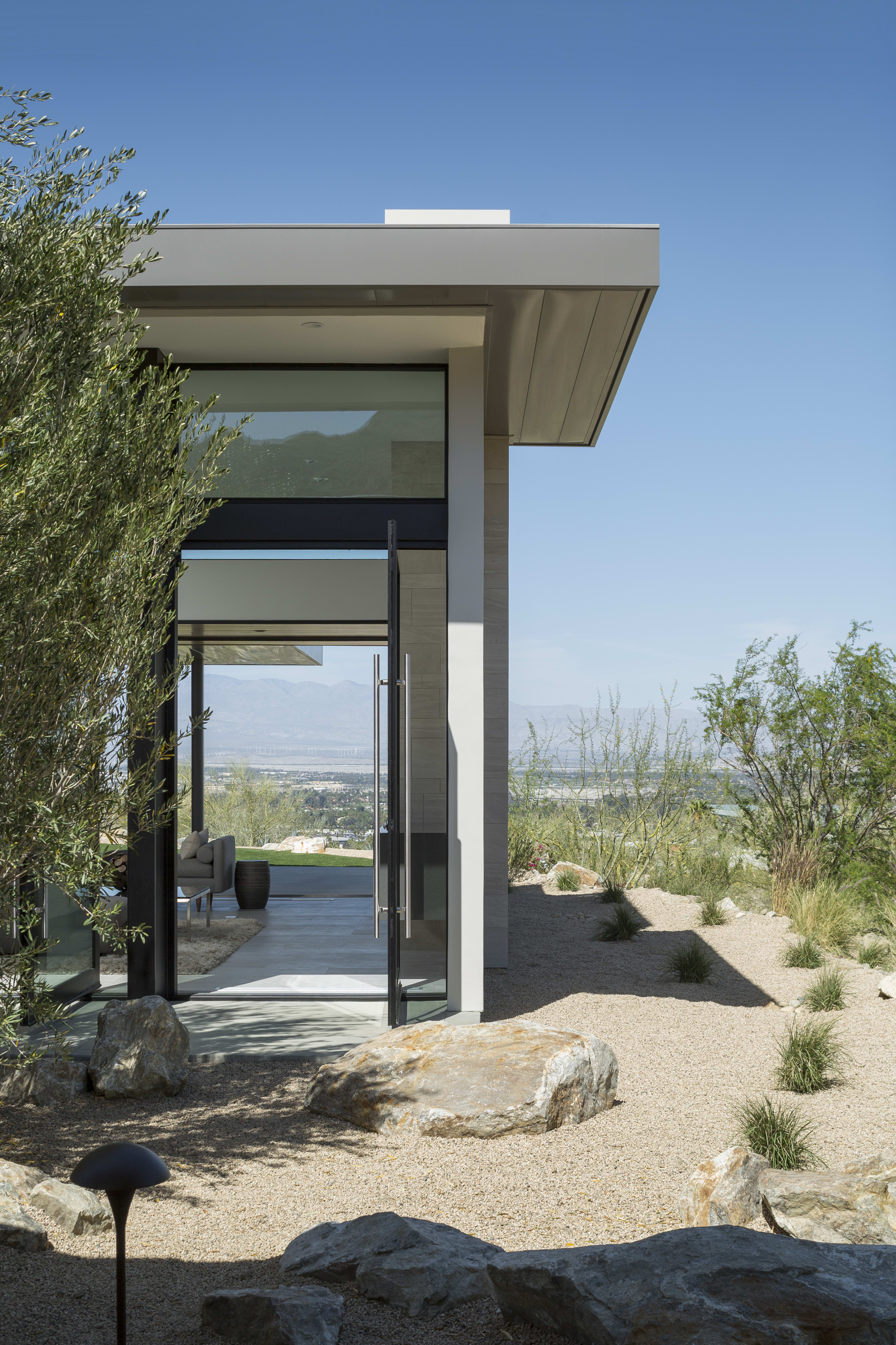 A large glass door leads into a modern home in the middle of a desert landscape