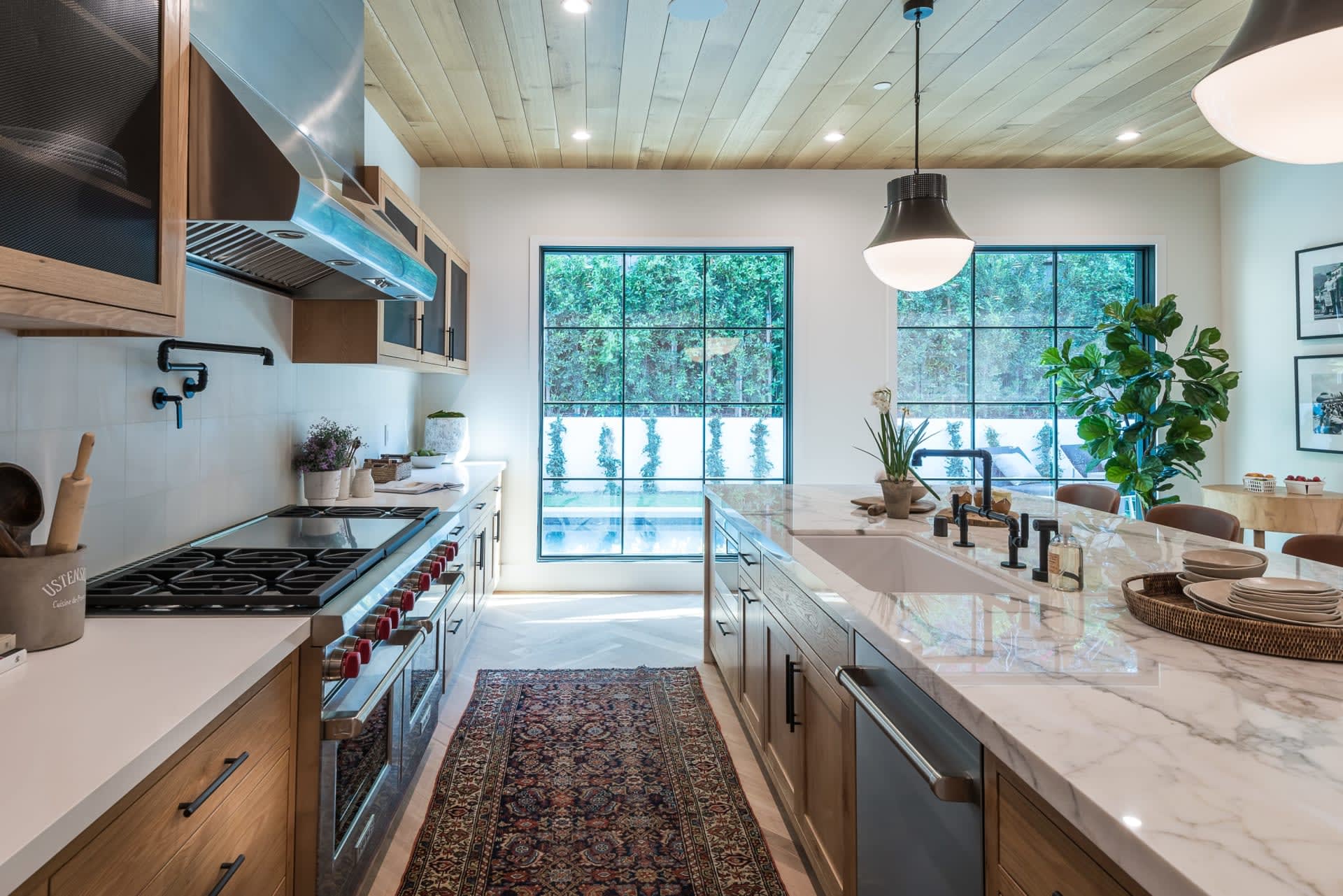A large kitchen with stainless steel appliances, wooden cabinets, a large island with a sink and faucet, and pendant lights.