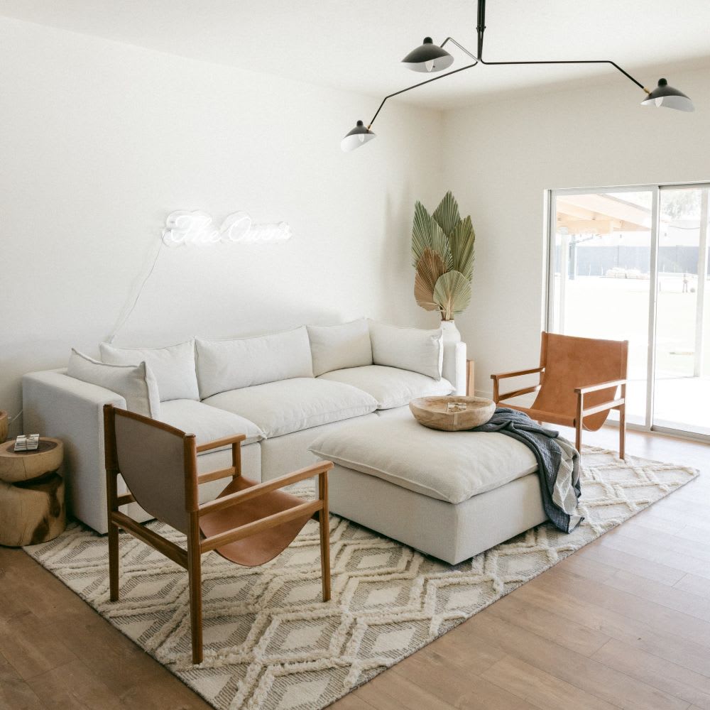 A living room with a couch, chairs, ottoman, and a neon sign on the wall