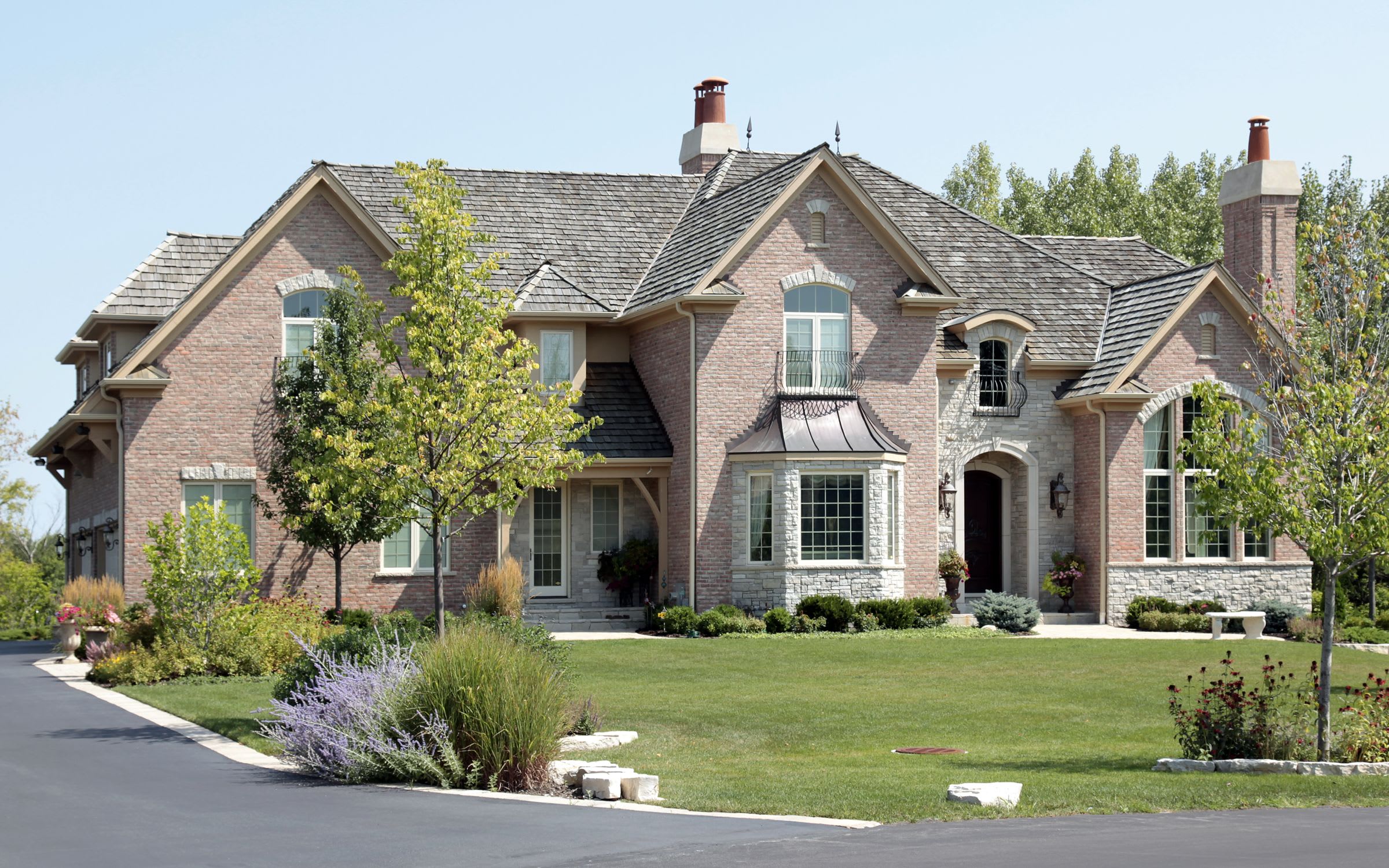 A two-story brick house with a covered porch and an open lawn with trees.