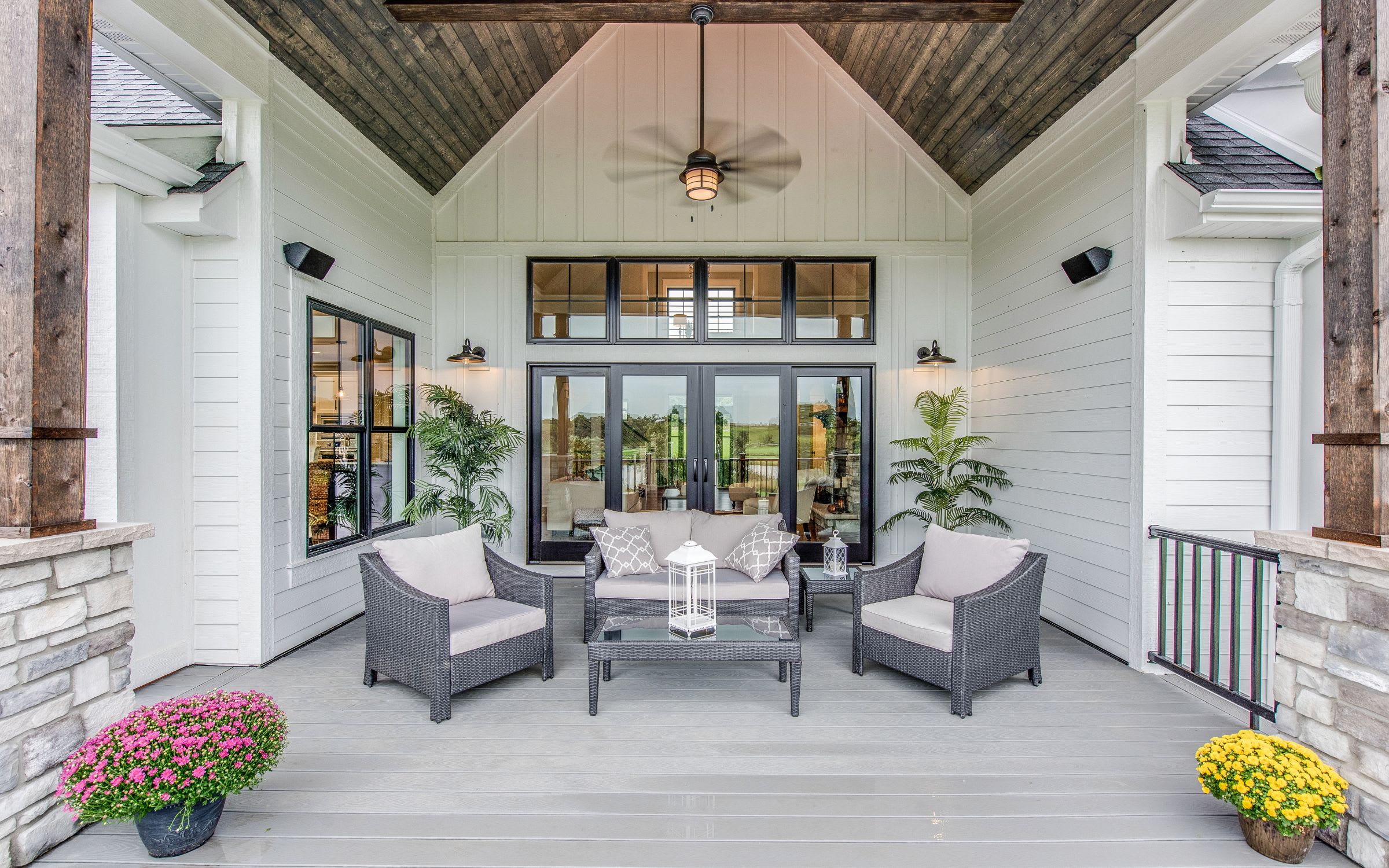 A covered porch with a ceiling fan sits amidst lush greenery.