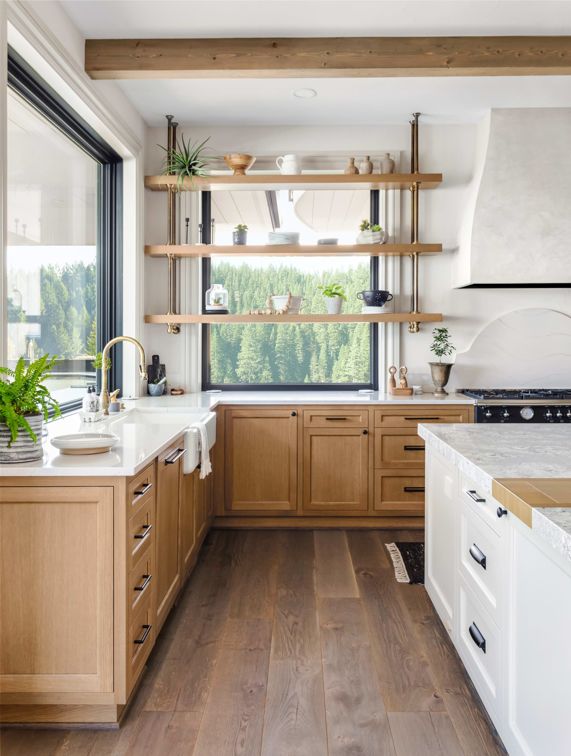 A modern kitchen with wooden cabinets, floating shelves, a countertop island, and large windows with outdoor views.