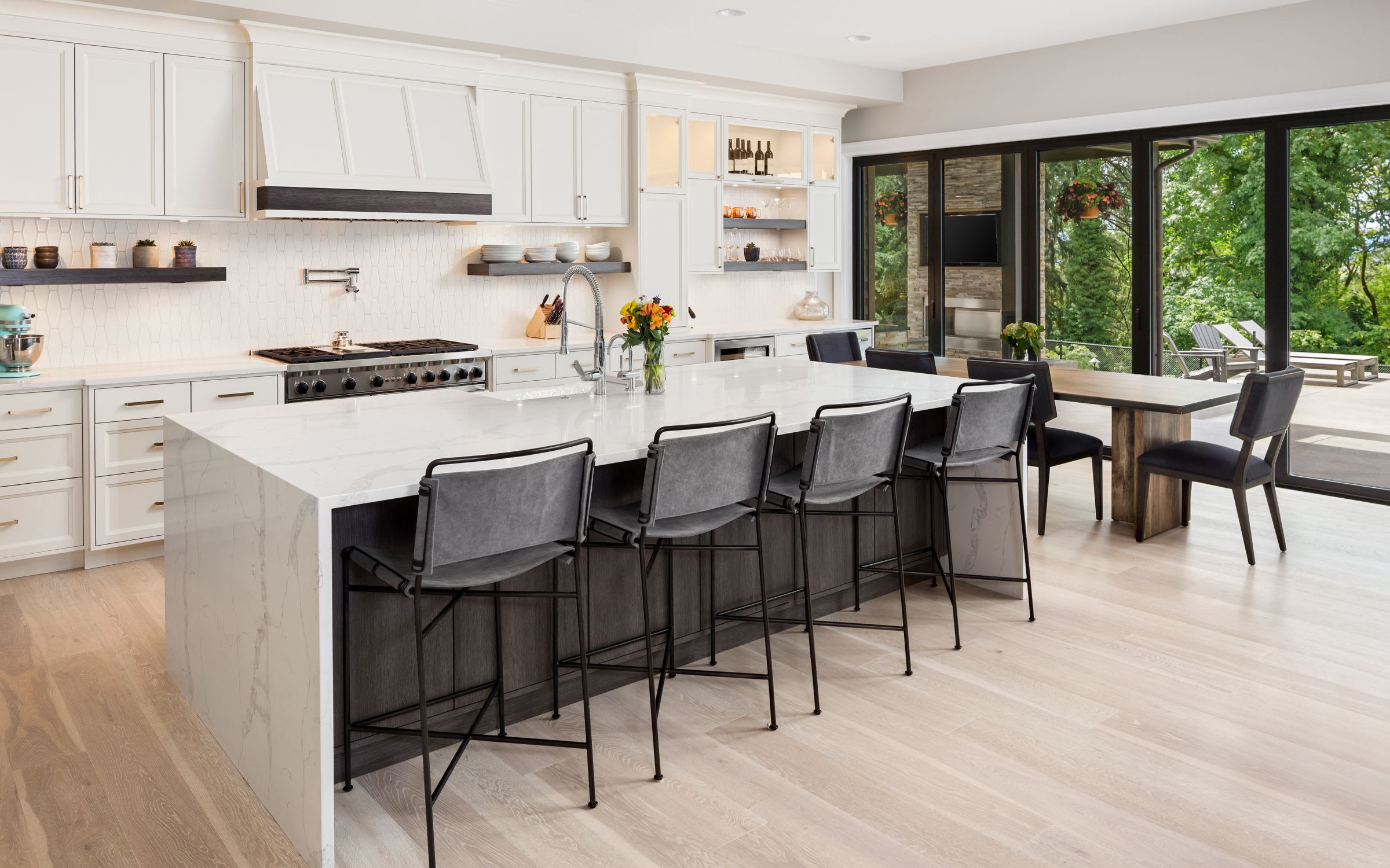 A modern kitchen with white cabinets, large white marble island and five black metal stools