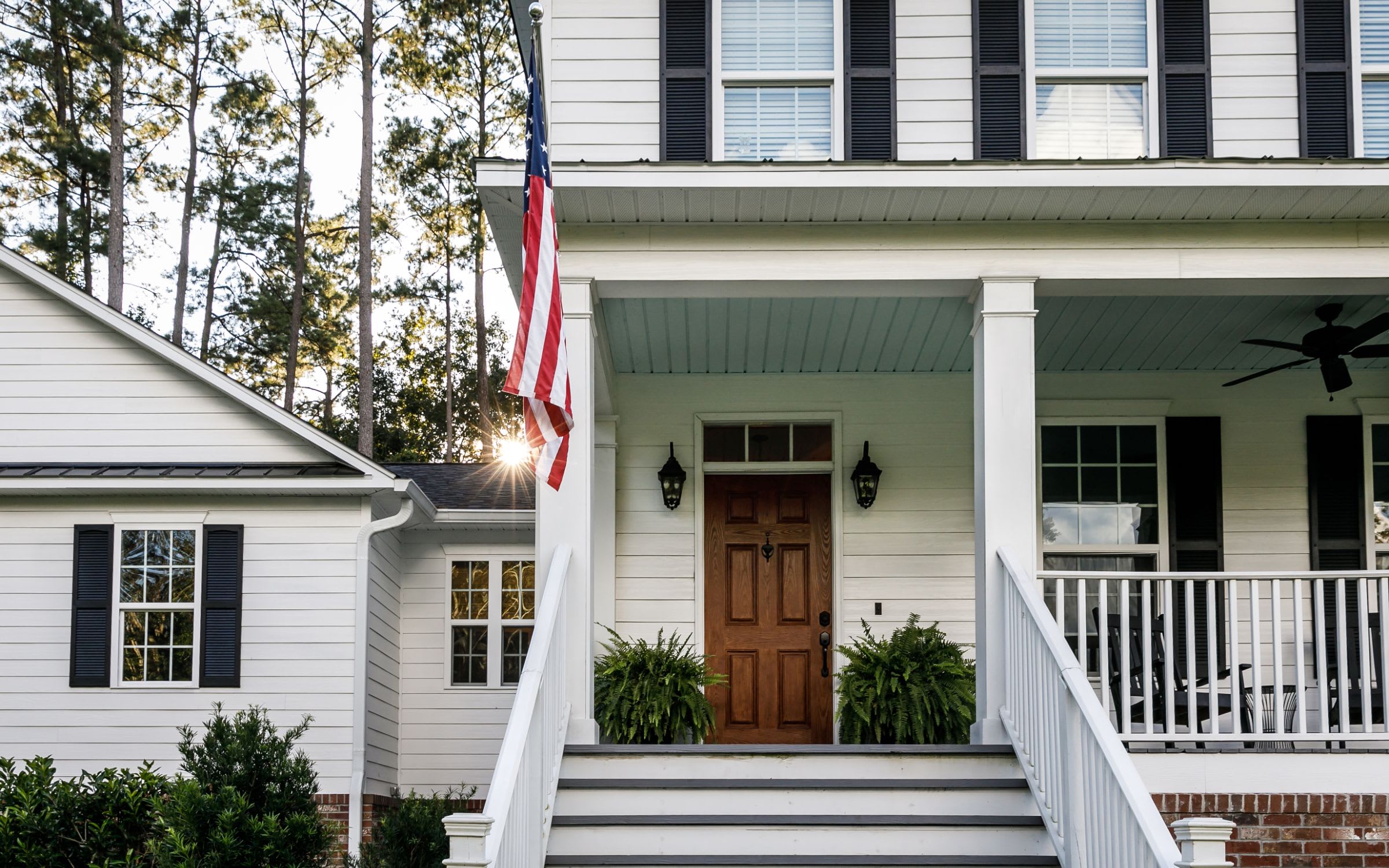 A rustic house with a wooden porch and an American flag. There are white rocking chairs on the porch.