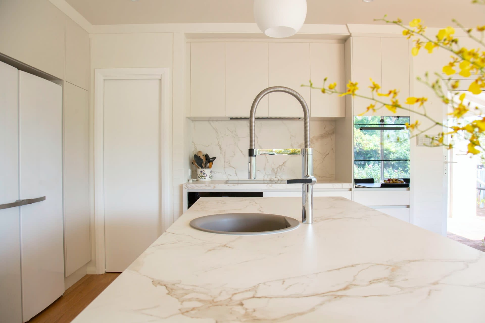 A modern kitchen with hardwood floors, a sink and faucet, light wood cabinets, and stainless steel appliances.