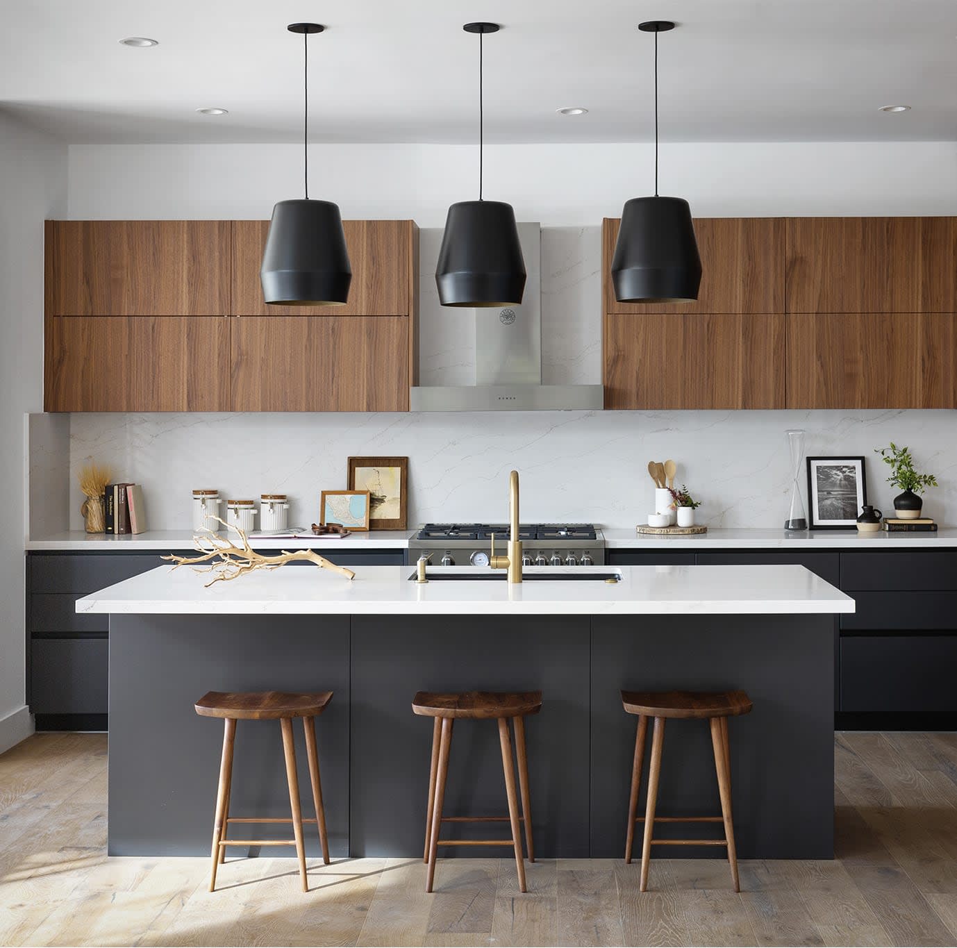 A kitchen with a large island and three stools, a stove, and a refrigerator