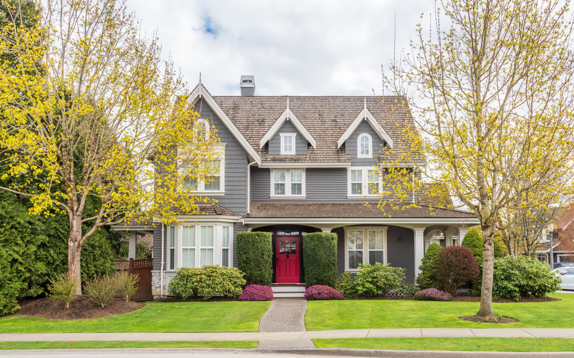 A gray two-story house with a red front door and a shingled roof