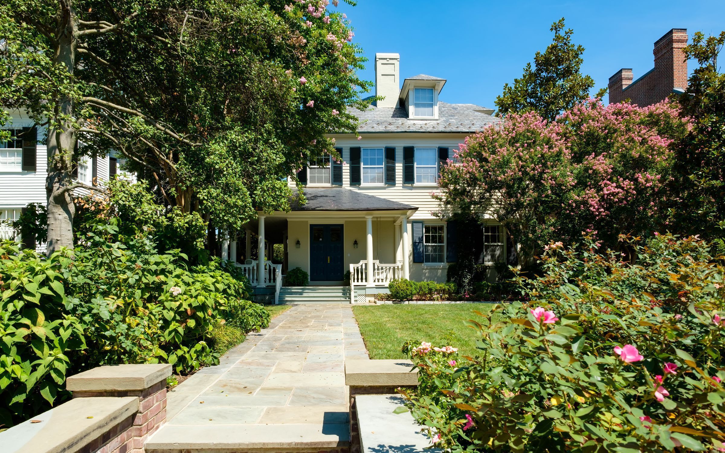 A stone walkway leading to a white house with a black door.