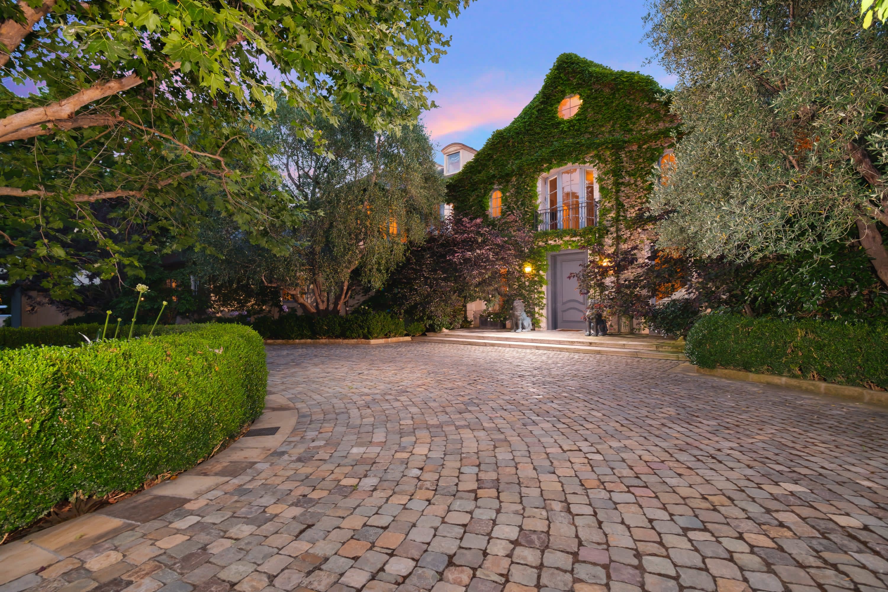 A brick driveway leading to a large house with ivy on the wall