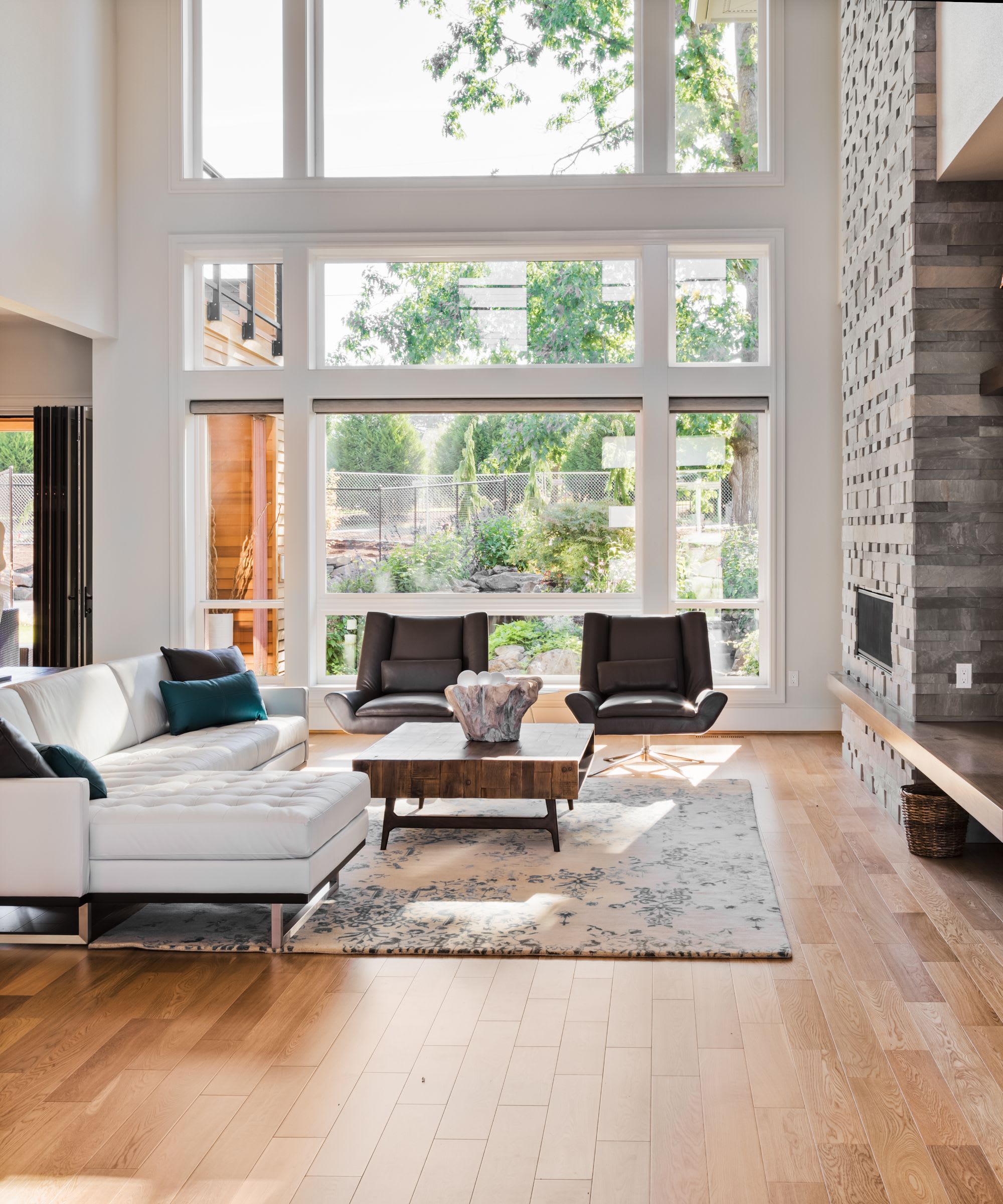 A living room with floor-to-ceiling windows, a couch, two chairs, a fireplace, and a coffee table in front of the couch.