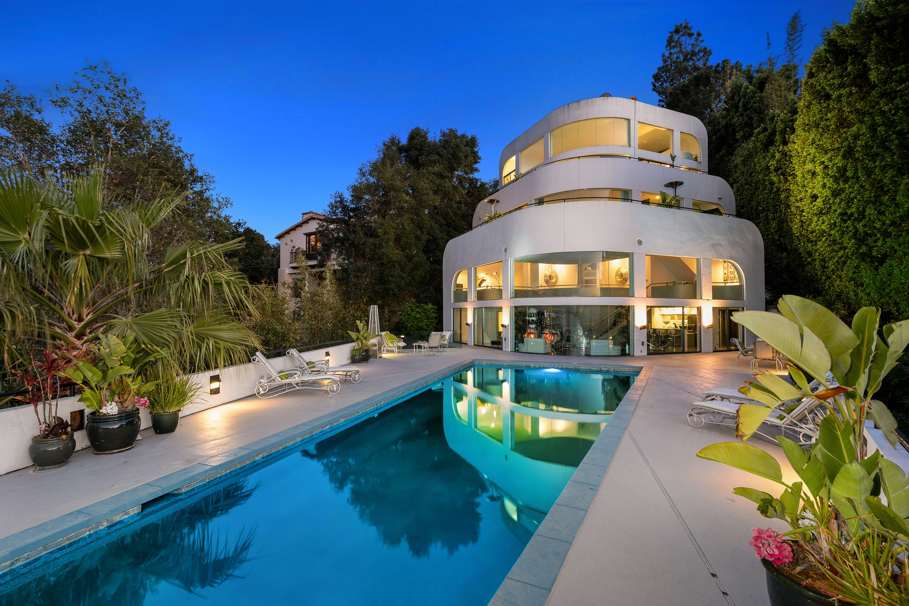 A large white house with a swimming pool in front of it. The house is surrounded by trees