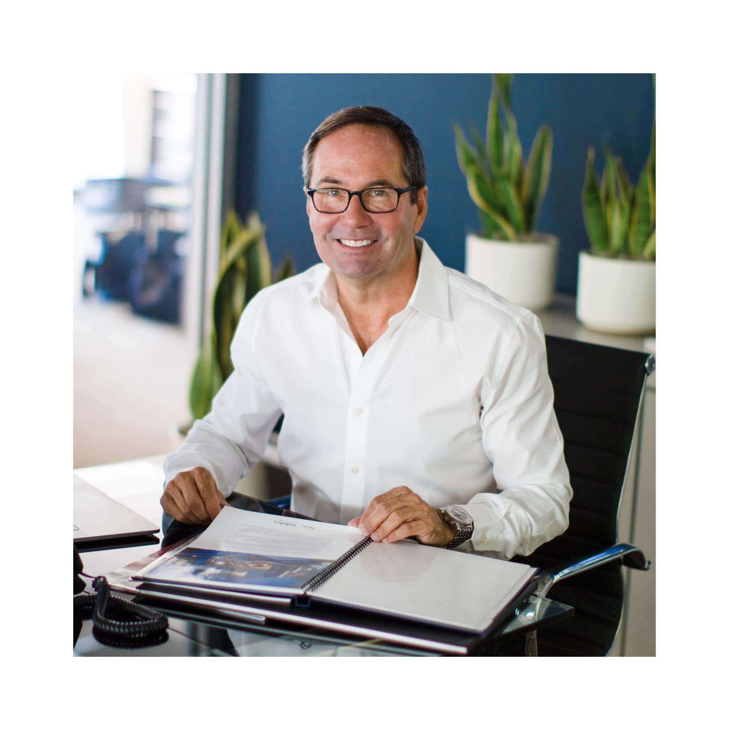 A photo of Gregg Fletcher sitting in an office chair with magazine on the desk