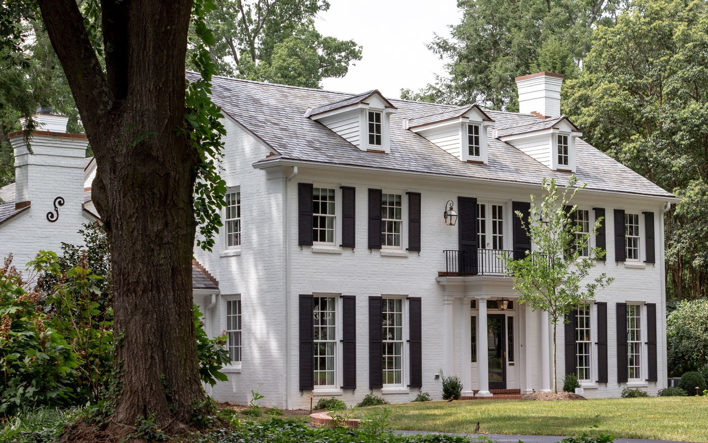 A modern house with a black roof, windows spanning the whole first floor, and a covered porch.