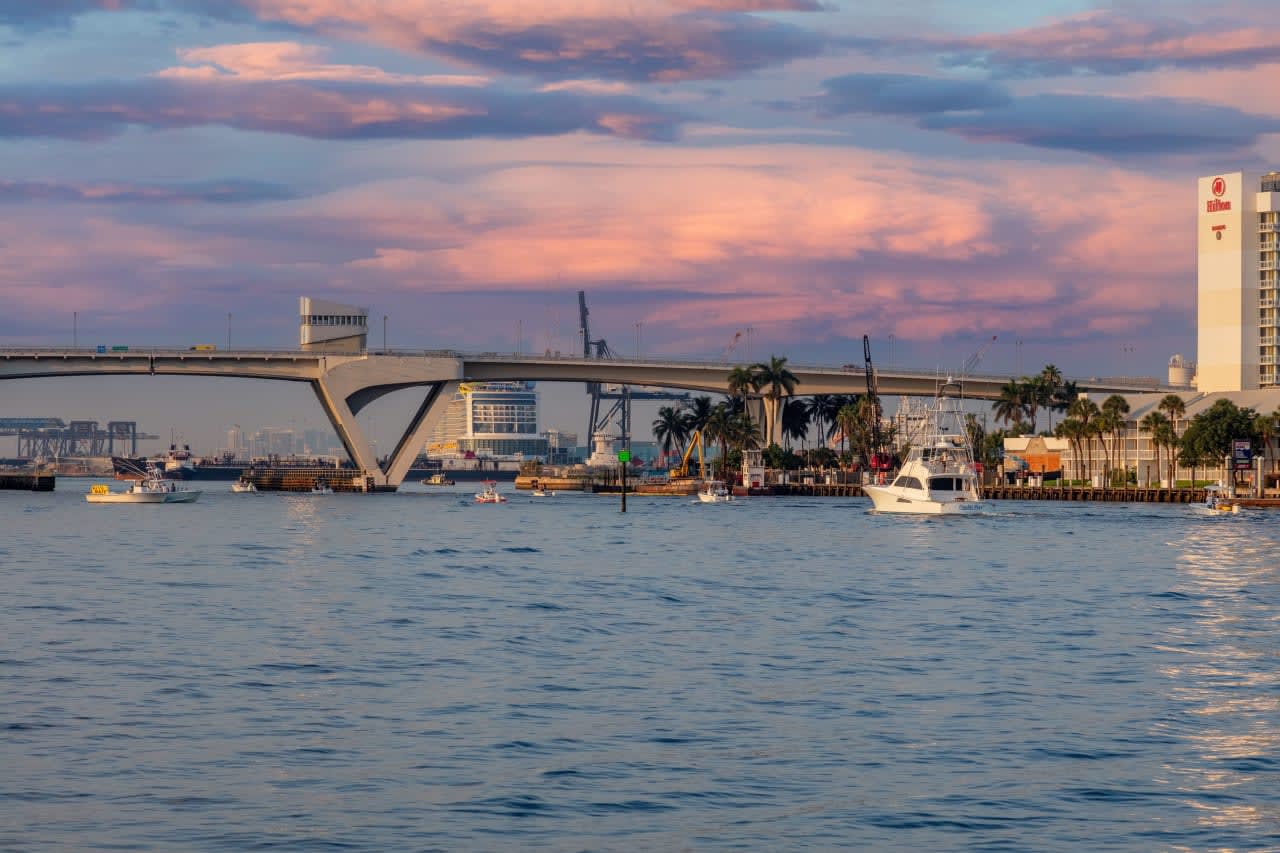 A group of boats floating on top of a body of water with a bridge in the background.